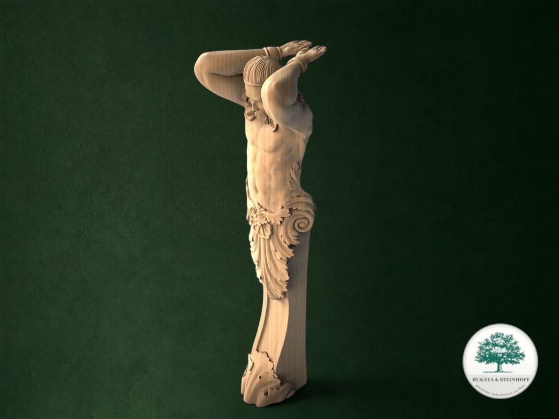 A wooden sculpture of a person with their arms raised, standing against a dark green background.