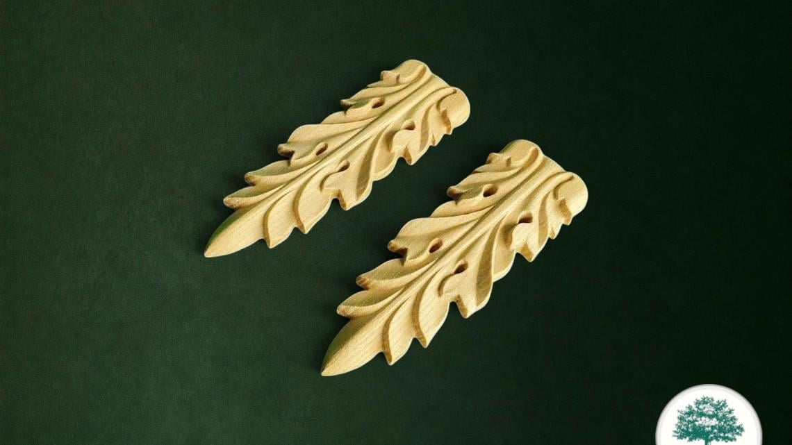 two intricately carved wooden leaf-like objects with a dark green background.