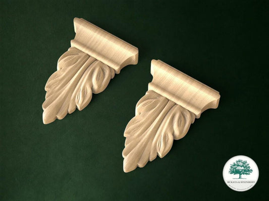 two ornate wooden ornaments with leaf-like designs, placed on a dark green background.