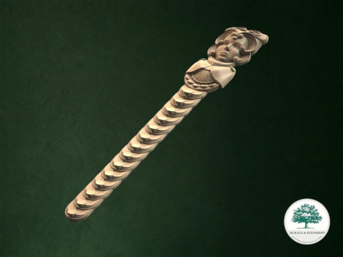 A decorative wooden object with a carved face and a row of small circles along its length, set against a dark green background.