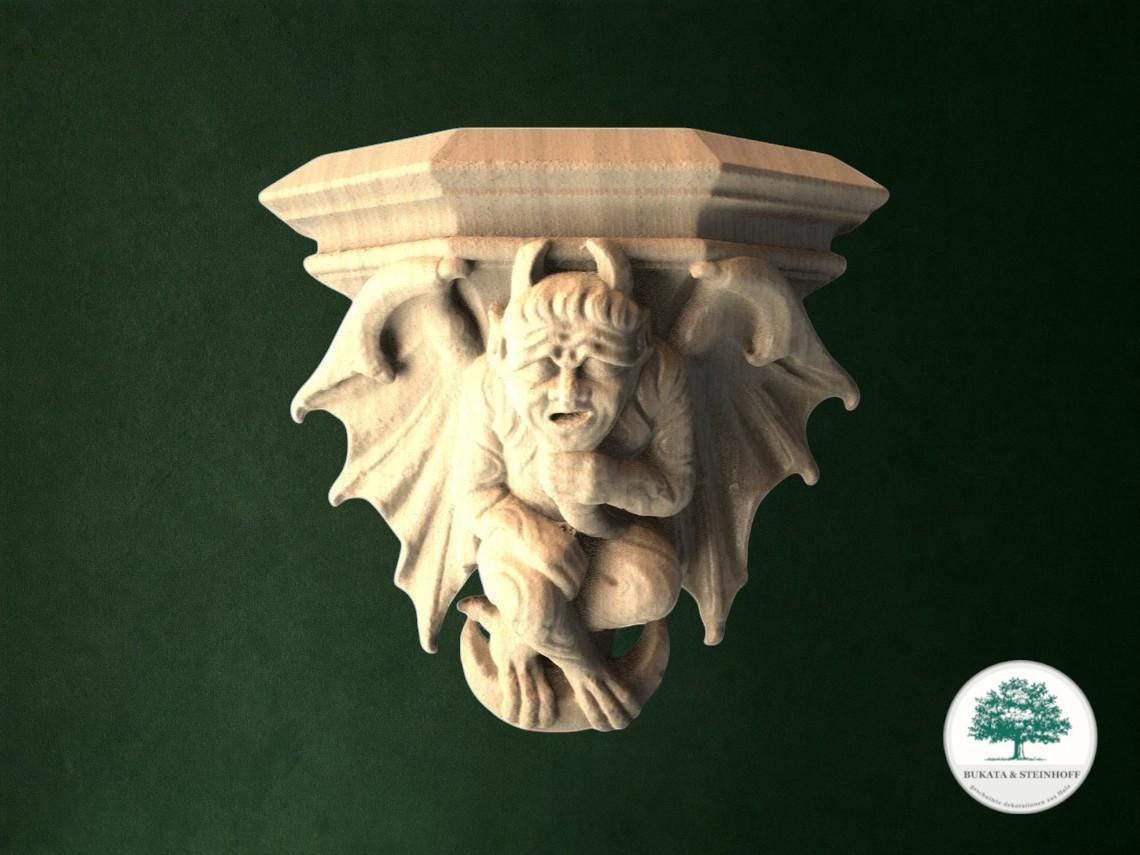 A carved wooden sculpture of a gargoyle figure with wings and horns, set against a dark green background.